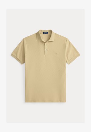 Beige kortermet polotrøye med to hvite knapper, ribbet krage og mansjetter, og subtil brodert logo på venstre bryst.