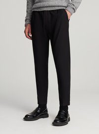 Pantaloni neri con vestibilità su misura, vita elasticizzata, tasche laterali e una texture liscia, abbinati a mocassini neri lucidi.