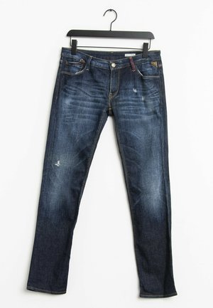 Ciemnoniebieskie jeansy slim fit z lekkim przetarciem i wyblaknięciem, wiszące na czarnym wieszaku na białym tle.