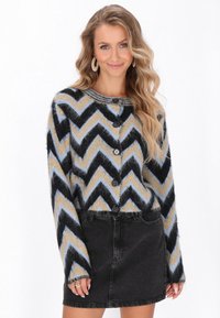 Langärmlige Strickjacke mit einem Zickzackmuster in Schwarz, Beige und Hellblau. Ausgestattet mit fünf Knöpfen und einer weichen Textur, kombiniert mit einem schwarzen Jeansrock.