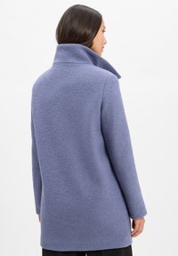 Maßgeschneiderter Wollmischmantel in Hellblau mit hohem Kragen, langen Ärmeln und einer leicht übergroßen Passform, der eine weiche, strukturierte Oberfläche aufweist.