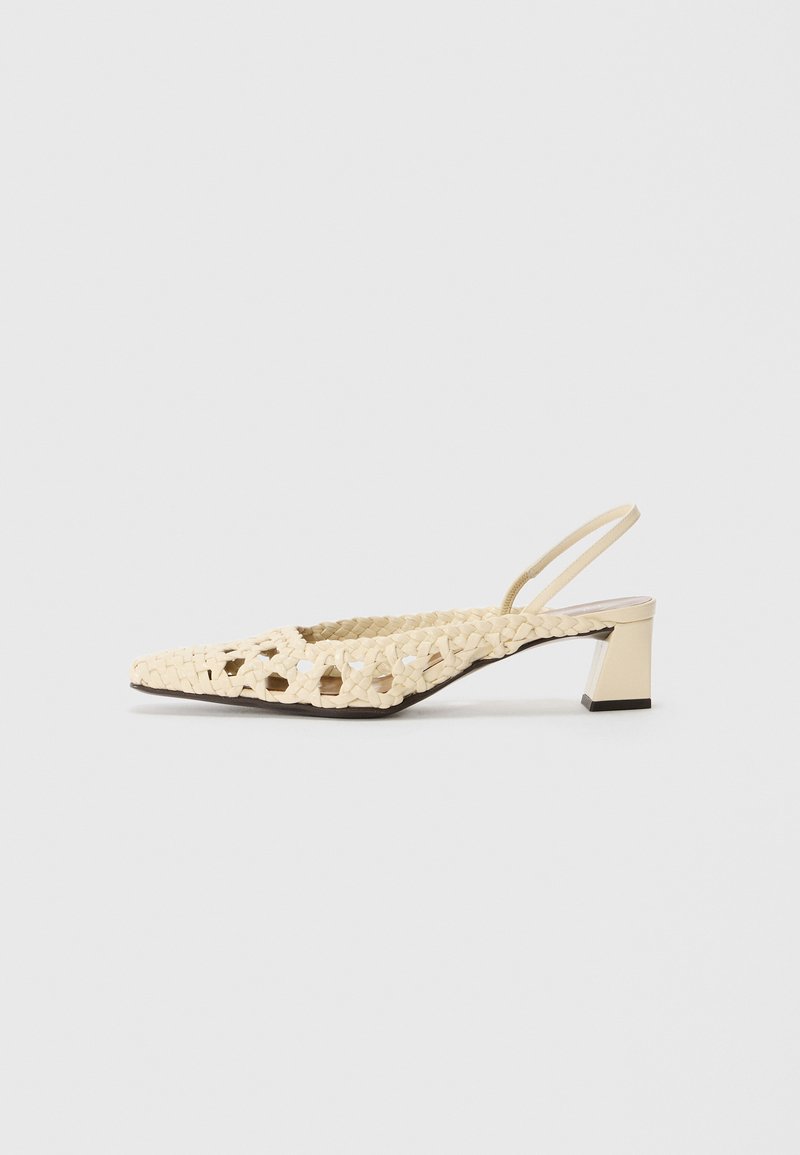 Zapato de slingback tejido en beige con punta afilada y tacón bajo cuadrado. La parte superior presenta patrones recortados y un acabado suave.