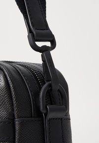 Bolso de cuero negro texturizado con cierre de cremallera. Cuenta con un clip negro mate y herrajes de correa para un attachment seguro.