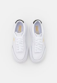 Białe sneakersy z gładkiej skóry, kontrastującym czarnym paskiem na pięcie, płaskimi sznurowadłami i złotym logo na boku.