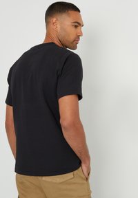 Schwarzes T-Shirt mit kurzen Ärmeln und Rundhalsausschnitt, aus strukturiertem Baumwollstoff gefertigt. Das Shirt hat einen lockeren Sitz und dezente Nahtdetails.