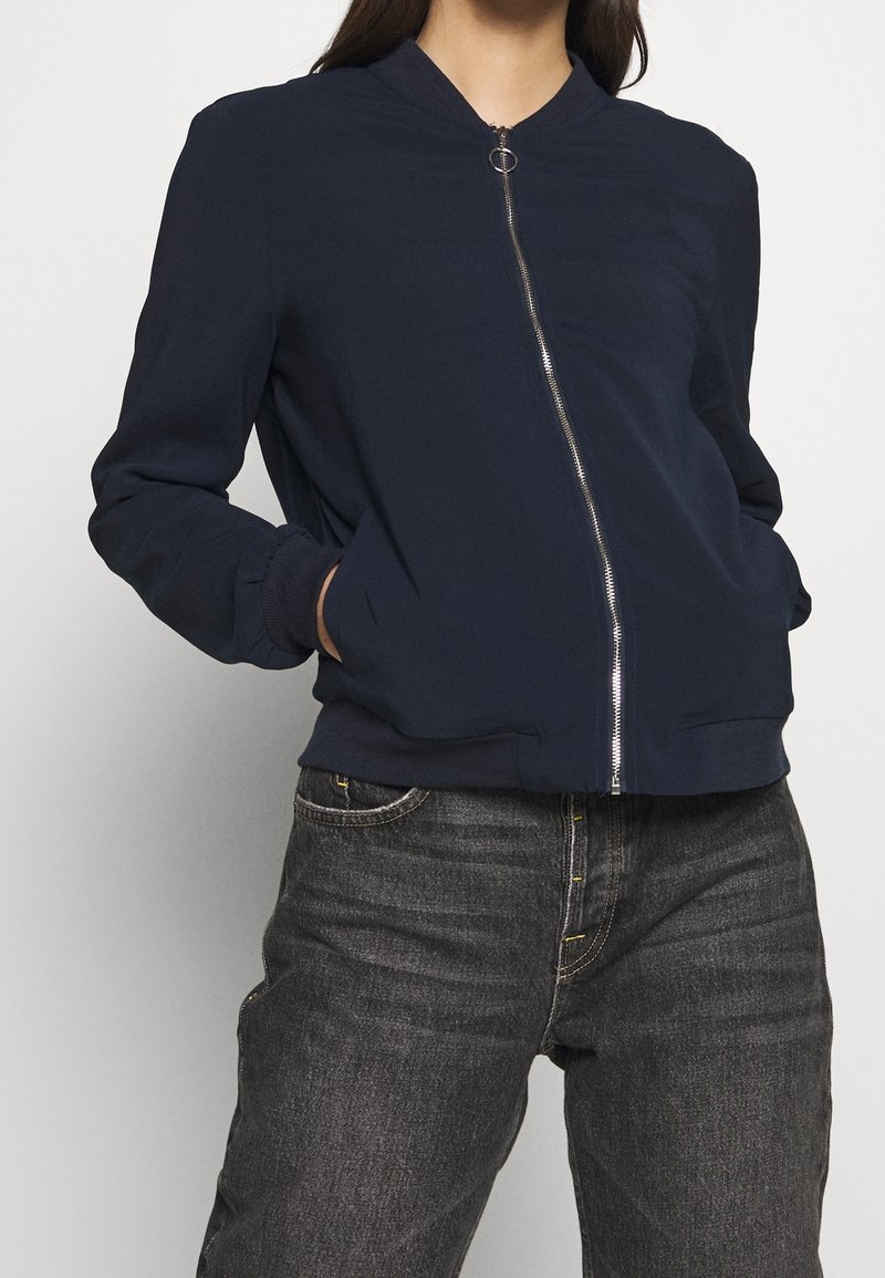 Mörkblå bomberjacka med framdragkedja, ribbade manschetter och nederkant, samt sidofickor. Slät tygkvalitet med en avslappnad passform.