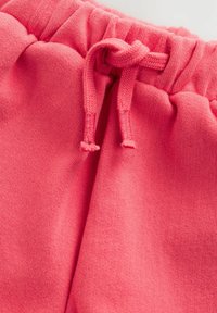 Roze katoenen trainingsbroek met een elastische tailleband en koord. De textuur is zacht en de stof heeft een gladde afwerking.