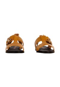 Tan leren sandalen met kruislings banden en een ronde metalen gesp. Open teen ontwerp, platte zwarte zool, minimale textuur en gestroomlijnde vorm.