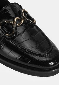 Zwarte gepatenteerde leren loafers met een krokodillenpatroon. Voorzien van een gouden en zwarte decoratieve kettingaccent. Platte zool en rondtote ontwerp.