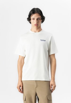 White cotton t-shirt with a crew neck and short sleeves. Features a blue Timberland logo on the left chest. Smooth texture, regular fit.