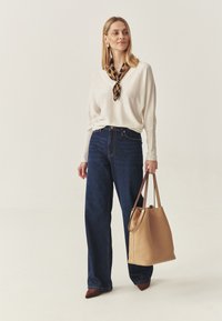 Pulover tricotat bej, blugi albaştri închişi cu talie înaltă şi o geantă tote din piele maro deschis. Eşarfă cu un model maro şi negru legată la gât. Pantofi maro.