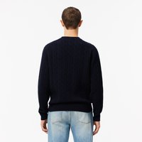 Marineblå strikkegenser med kabelmønster, rund halsutringning og ribbede mansjetter og kant. Båret over lyseblå jeans, sett fra baksiden.