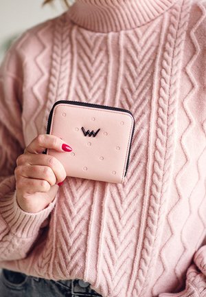Light pink leather wallet with circular embossed patterns, black zipper, and logo displayed on the front, held against a pink textured sweater.