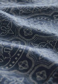 Marine blå stof med et detaljeret hvidt paisley-mønster, med struktureret væv og indviklede designs gennem materialet.