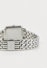 Silberner Edelstahlarmbanduhr mit rechteckigem Ziffernblatt, verbundenem Armband und einer Schließe, die auf der Innenseite das "COACH"-Logo trägt.