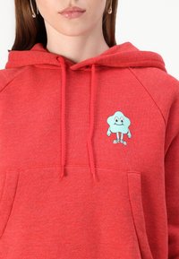 Red hoodie made of soft fabric, featuring a front pocket and a turquoise cartoon character embroidered on the chest with a smiling expression.