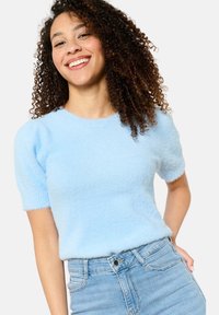 Light blue, fuzzy short-sleeve sweater with a round neckline and ribbed cuffs, paired with high-waisted denim jeans.