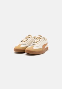 Pair of beige and tan low-top sneakers with brown rubber soles and laces, displayed on a white background.