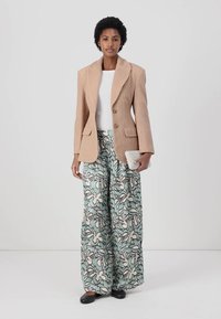 Blazer textured in marrone chiaro con colletto ampio, abbinato a pantaloni a gamba larga con un motivo floreale in menta, nero e crema. Ballerine nere.