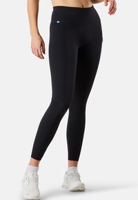 Leggings noirs en tissu léger et extensible, dotés d'une taille haute, d'une poche zippée et d'un petit logo sur la taille.