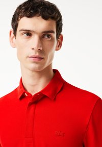 Röd polo skjorta i strukturerad bomull med klassisk krage, försedd med två knappar och en liten broderad logotyp på vänster bröst.