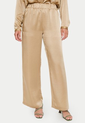 Beige, weit geschnittene Hose aus glattem, glänzendem Stoff mit elastischem Bund. Verfügt über schmal zulaufende Knöchel und einen lässigen Schnitt.