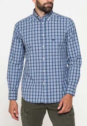 Uomo che indossa una camicia a quadri blu e bianca con maniche lunghe e pantaloni cargo verde oliva.