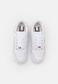 Bílé tenisky z hladké kůže s perforacemi, plochými tkaničkami, visačkou s logem a jemnými oranžovými akcenty podél okrajů.