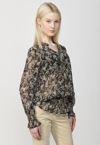 Blusa nera a fiori con maniche lunghe e orlo arricciato. Tessuto leggero e trasparente con un delicato motivo di fiori bianchi e dorati.
