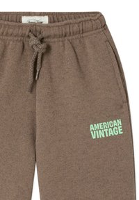 Pruunid dressipüksid, millel on elastne vöökoht ja nöör, ülal vasakul reielosas mintrohelise värviga kiri "AMERICAN VINTAGE".