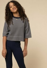 Grijs gestreept cropped top met brede mouwen, gecombineerd met marineblauwe leggings. Opvallende details zijn het logo op de top en de gladde stoftextuur.