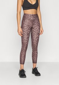 Καφέ κολάν με λεοπάρ σχέδιο και ψηλή μέση, κατασκευασμένο από ελαστικό ύφασμα, σε συνδυασμό με μαύρα αθλητικά παπούτσια και μαύρο αθλητικό σουτιέν.