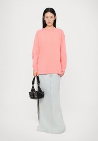 Bright pink oversized sweatshirt with long sleeves, featuring a discreet logo; paired with a light blue denim skirt and a black handbag with studs.