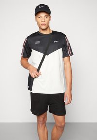 Camiseta Nike en blanco y negro, con un diseño de chevron, un logo y acentos a rayas en las mangas. Combinada con pantalones cortos negros y una gorra.