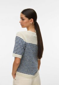 Pull en tricot avec un motif rayé crème et marine, manches courtes, bordures côtelées et coupe décontractée. La texture semble douce et confortable.