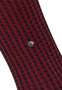 Rot-schwarzes Hahnentrittmuster mit glatter Textur, das ein silbernes, rundes Emblem mit eingraviertem Text zeigt.