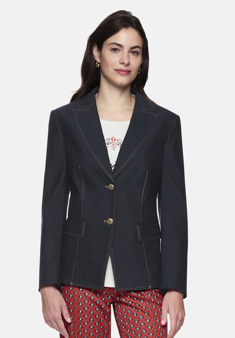 Navy blazer with a tailored fit, featuring gold-tone buttons, contrasting stitching, and two front pockets. Worn over a light-colored top.