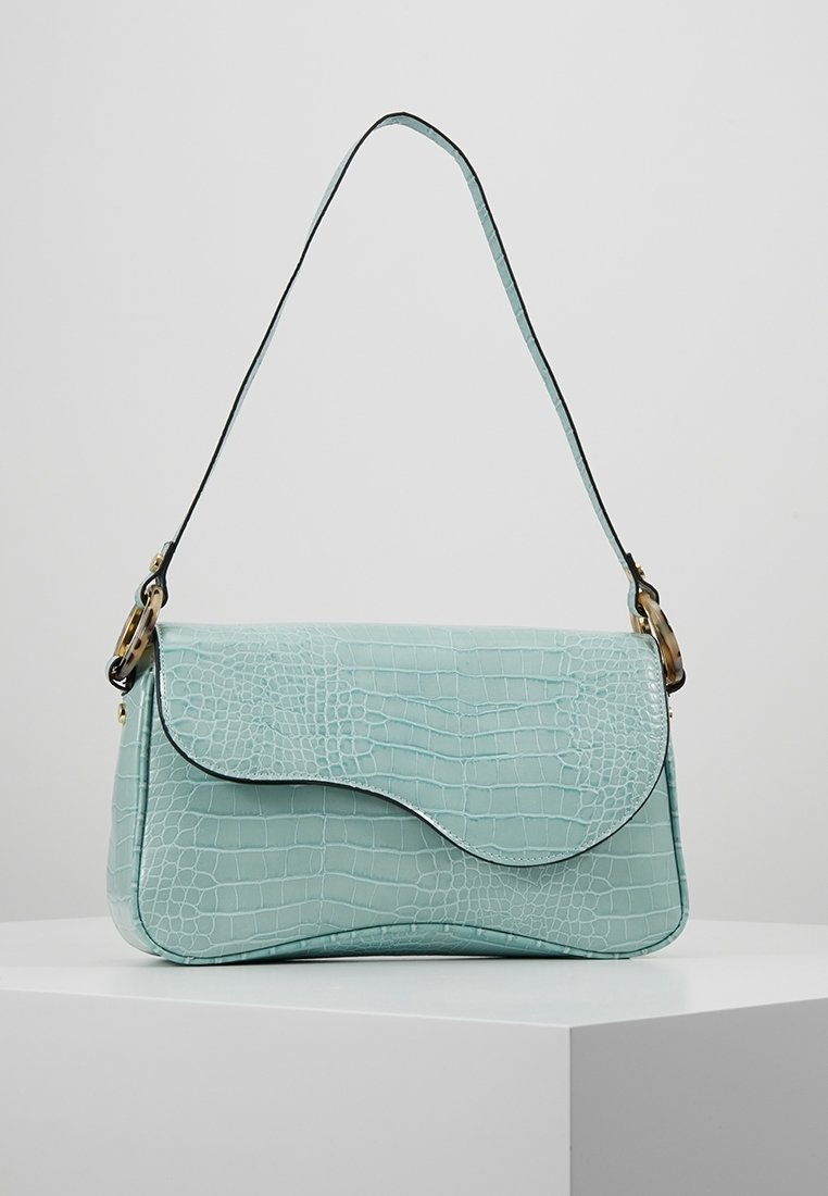 Sac à main en cuir bleu clair à texture crocodile avec rabat incurvé et bandoulière unique, posé sur une surface blanche.