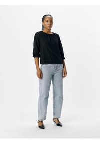 Black textured top with three-quarter sleeves, paired with light blue straight-leg jeans and black pointed-toe heels.