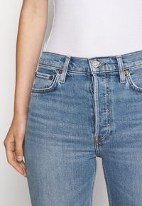 Jeans de mezclilla azul claro con cintura alta, que cuentan con cinco bolsillos, costuras en contraste y un cierre de botón plateado en la parte delantera.
