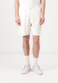 White, textured shorts with a subtle embossed pattern. Elastic waistband with drawstring. Paired with white sneakers and socks.