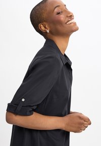 Zwart shirt met kraag en opgerolde mouwen, met een gladde textuur en een subtiele glans. Minimalistisch ontwerp zonder zichtbare patronen.