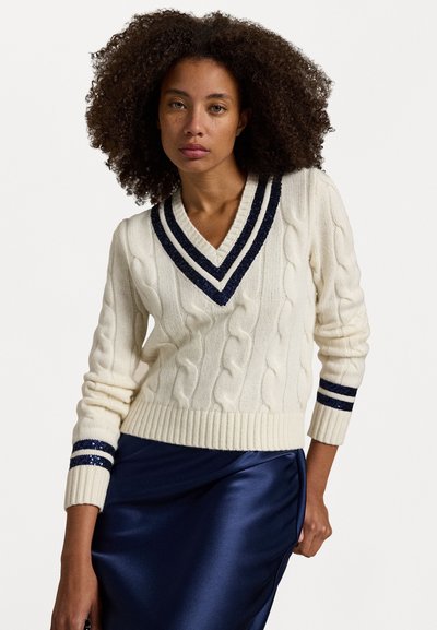 Pull en tricot torsadé crème avec un col en V et des accents rayés navy sur les manches. Présente des poignets et un ourlet côtelés, mettant en valeur un tissu texturé.