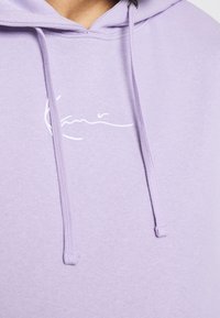 Vaaleanpunertava huppari, jossa on vetonarut. Rinnan kohdalla valkoinen kirjailtu kuvio. Valmistettu pehmeästä kankaasta, tarjoaa rentoa ilmettä.