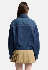 Kurtka dżinsowa w ciemnoniebieskim kolorze z klasycznym kołnierzem, luźnym krojem i plisowaną jasnobrązową spódnicą widoczną na dole, z pionowymi teksturowanymi liniami.