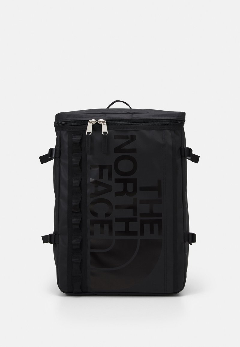 Sac à dos noir de forme carrée avec fermeture éclair sur le dessus, sangles latérales et grand logo vertical "The North Face" à l'avant.
