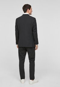 Zwarte op maat gemaakte pak met een recht gesneden jas en broek. Heeft een witte kraag en een minimalistisch ontwerp, gecombineerd met witte sneakers.