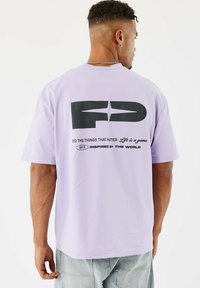 Lavender T-shirt met korte mouwen van katoen, voorzien van een grote zwarte graphic "FD" en tekst in contrasterende kleuren op de achterkant.
