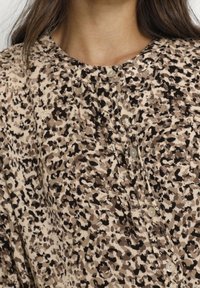 Leopard print blouse with brown, beige, and black patterns; features a rounded neckline and pearl buttons along the front. Soft fabric texture.