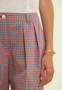 Pantalons en tartan avec un motif à carreaux rouge, bleu et blanc. Taille haute avec des plis à l'avant et une fermeture à bouton. Texture de tissu lisse.